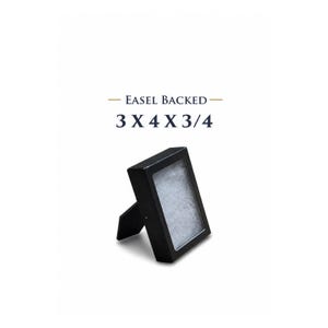 May include: A black easel-backed display case, 3 x 4 x 3/4 inches, with a rectangular opening. The case is angled, supported by a small stand. The interior appears to be filled with a white, textured material. The text "EASEL BACKED" and "3 X 4 X 3/4" are above the case.