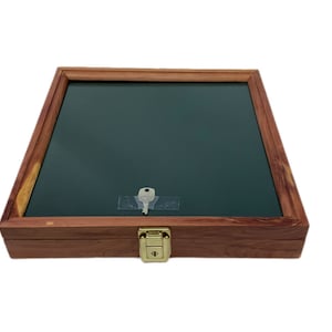 May include: A wooden display case with a dark green interior and a glass top. The case has a rectangular shape with a hinged lid and a brass-colored clasp. A key is taped to the glass.