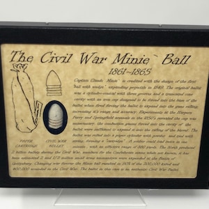 May include: A framed display with a close-up of a Civil War Minie Ball, a type of bullet used in the American Civil War. The display includes a description of the bullet's history and design. The text reads "The Civil War Minie Ball 1861-1865".