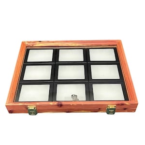 Op de afbeelding: Een houten vitrine met een glazen bovenkant en negen compartimenten. De behuizing is gemaakt van roodbruin hout met een rechthoekige vorm en een messing sluiting. Elk compartiment heeft een zwart frame en een wit interieur.