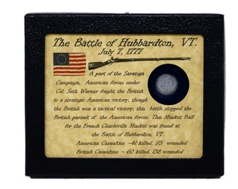 May include: A framed display with a musket ball from the Battle of Hubbardton, VT. The display features a small American flag, a musket, and text describing the battle. The text reads: "The Battle of Hubbardton, VT. July 7, 1777. A part of the Saratoga Campaign, American forces under Col. Seth Warner fought the British to a strategic American victory, though the British won a tactical victory, this battle stopped the British pursuit of the American forces. This Musket Ball for the French Charleville Musket was found at the Battle of Hubbardton, VT. American Casualties ~41 killed, 95 wounded. British Casualties ~60 killed, 138 wounded."