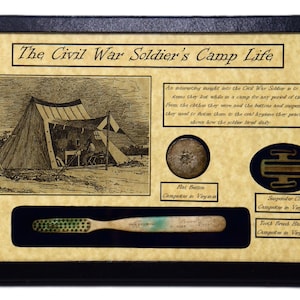 May include: A framed display with a vintage illustration of a Civil War soldier's camp life. The display includes a toothbrush, a suspender clip, and a flat button. The text on the frame reads "The Civil War Soldier's Camp Life".