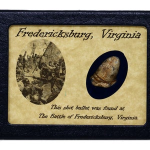 May include: A black box with a tan background containing a Civil War era bullet. The text on the box reads "Fredericksburg, Virginia" and "This shot bullet was found at The Battle of Fredericksburg, Virginia."