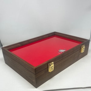 May include: A wooden display case with a red velvet interior and gold-colored clasps. The case is closed and has a dark wood finish.