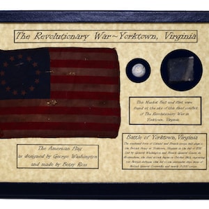 Könnte beinhalten: Eine gerahmte Darstellung mit einer Nachbildung der amerikanischen Flagge mit 13 Sternen in einem Kreis, einer Musketenkugel und einem Feuerstein. Der Text lautet "The Revolutionary War~Yorktown, Virginia" und "The American Flag as designed by George Washington and made by Betsy Ross". Der Text beschreibt auch die Schlacht von Yorktown, Virginia.