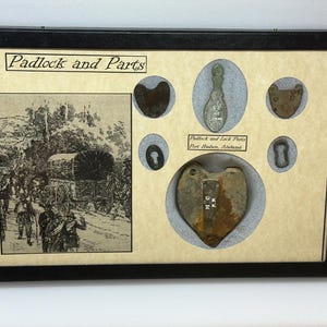 Puede incluir: Una exhibición enmarcada titulada "Padlock and Parts" con componentes de cerraduras antiguas y una ilustración histórica. La exhibición incluye varias partes de cerraduras y un candado en forma de corazón.