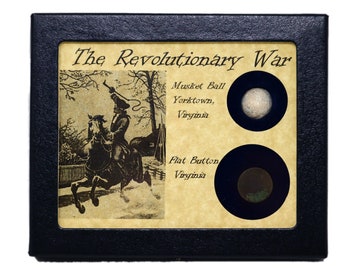 May include: A black leather box with a tan background and a picture of a soldier on horseback. The text "The Revolutionary War" is at the top of the box. There are two round compartments with a musket ball and a flat button inside.