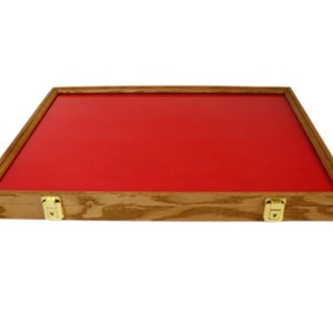 May include: A wooden display case with a red interior. The case has a rectangular shape with a light brown wooden frame and gold-colored latches. The interior is a vibrant red color.