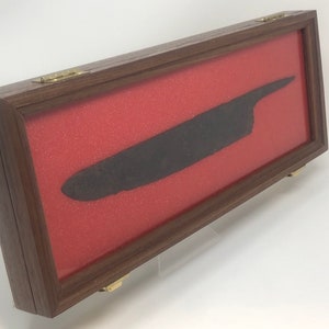 May include: A dark brown wooden display case with a glass top and a red velvet lining. A long, black metal blade is displayed inside the case.