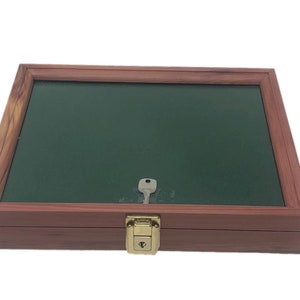 Puede incluir: Una vitrina de madera con un interior de fieltro verde y una cerradura de latón. La vitrina tiene una tapa con bisagras y es ideal para exhibir objetos pequeños.