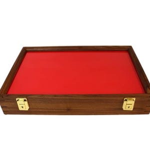 May include: A wooden display case with a red felt lining and brass clasps. The case is closed and sitting on a white surface.