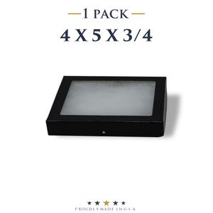 Puede incluir: Una caja de exhibición negra con una ventana transparente, que mide aproximadamente 10 x 13 x 2 cm. El texto "-1 PACK-" y las dimensiones se muestran encima de la caja. La parte inferior de la imagen dice "PROUDLY MADE IN U.S.A." con iconos de estrellas.