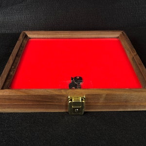 May include: A wooden display case with a red velvet interior and a brass latch. The case is closed and has a glass top.