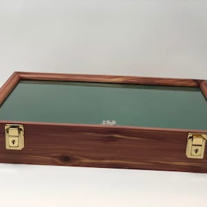 May include: A wooden display case with a green felt interior and two brass latches. The case is closed and sitting on a white surface.