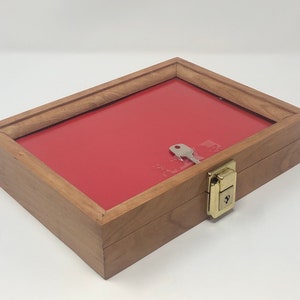 May include: A wooden display case with a red velvet interior and a brass lock and key. The case is closed and the key is in the lock.