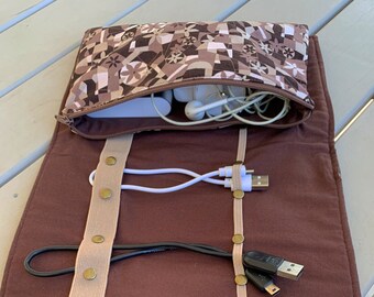 Könnte beinhalten: Eine braune Stoffrolle mit beigefarbenen Gummibändern und goldenen Druckknöpfen. Die Rolle ist geöffnet und enthält verschiedene Kabel und Drähte, die ordentlich darin verstaut sind.