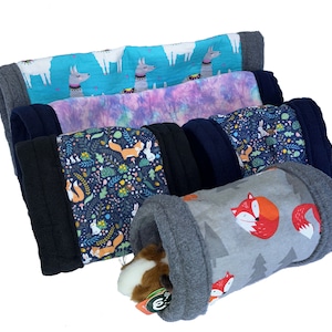May include: A selection of pet tunnels in different patterned fabrics. Designs include llamas, tie-dye, foxes, and woodland creatures. The tunnels are gray, blue, and black, with a guinea pig inside one.