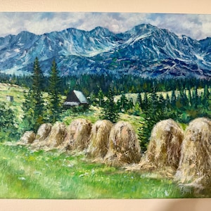 May include: Oil painting of a mountain landscape with a row of hay bales in the foreground. The mountains are blue and white, with a forest of green trees and a small cabin. The sky is cloudy.