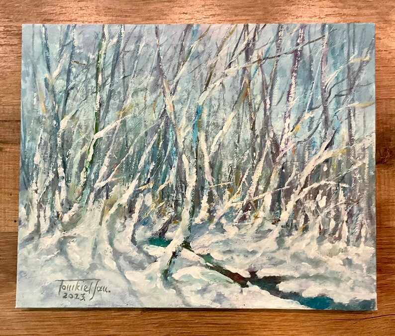 Puede incluir: Una pintura que representa una escena de bosque nevado con un peque&ntilde;o arroyo que lo atraviesa. Los &aacute;rboles est&aacute;n desnudos y cubiertos de nieve, y el cielo es de un azul claro. La pintura est&aacute; firmada "Tourkiel" y fechada "2023."