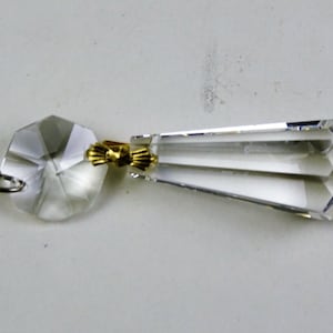 Puede incluir: Un prisma de cristal transparente para lámpara de araña con un conector dorado y un bucle colgante. El prisma es facetado y tiene forma de lágrima.