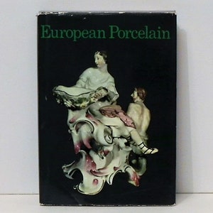 May include: A book cover with the title "European Porcelain" in white text on a black background. The cover features a porcelain figurine of a woman and a man, with the woman holding a bowl and the man sitting on a decorative base.