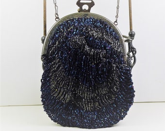 Puede incluir: Un bolso vintage con cuentas de color azul oscuro con un acabado iridiscente. El bolso tiene un marco de metal y una correa de cadena. El diseño de cuentas crea una superficie texturizada. Un accesorio clásico.