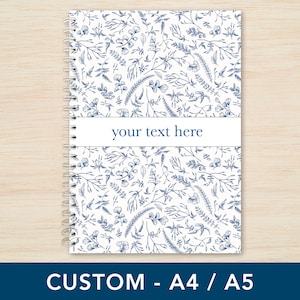 May include: A white notebook with a blue floral pattern and a blue stripe across the middle that says "your text here". The notebook has a spiral binding.