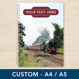 May include: A spiral bound notebook with a custom cover featuring a vintage steam train with smoke billowing from the chimney. The train is travelling on a track through a green field with trees in the background. The cover also includes the text "YOUR TEXT HERE" in a red banner.