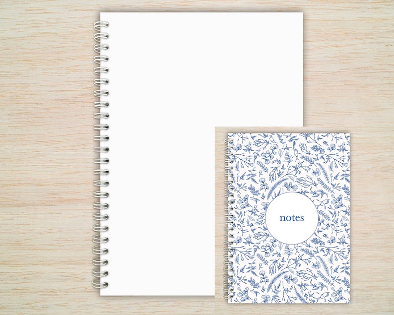 May include: Two spiral bound notebooks. The larger notebook has a white cover. The smaller notebook has a white cover with a blue floral pattern and the word "notes" in a circle.