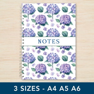 May include: A white notebook with a spiral binding and a floral pattern featuring purple hydrangeas and green leaves. The notebook has the word "NOTES" printed in blue on the front cover. The notebook is available in three sizes: A4, A5, and A6.