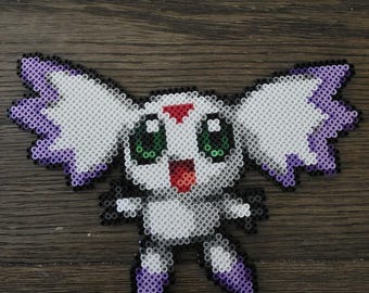 May include: A handmade pixel art figure of a cartoon character, created with colorful plastic beads. The figure has white, purple, black, red, and green details. It features large ears, green eyes, and a smiling mouth. The figure is placed on a wooden surface.