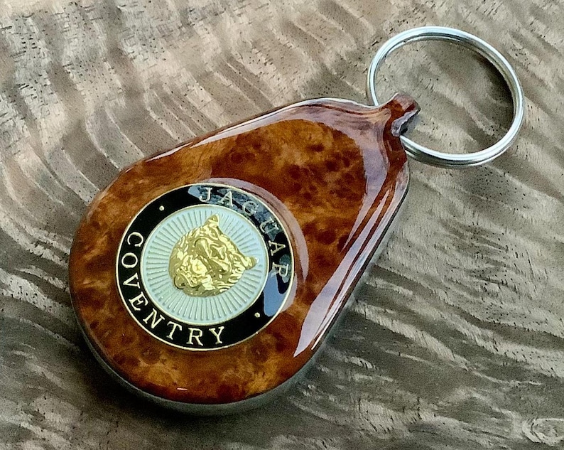 May include: A teardrop-shaped keychain featuring a polished brown burl wood finish and a circular emblem. The emblem displays a gold jaguar head on a white background, surrounded by a black border with the text JAGUAR COVENTRY in gold letters.