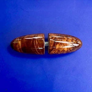 Puede incluir: Un tapón de botella de madera de dos piezas con un mecanismo de tornillo. El tapón está hecho de madera pulida con un rico patrón de vetas marrones. Las dos mitades están conectadas por un tornillo plateado.