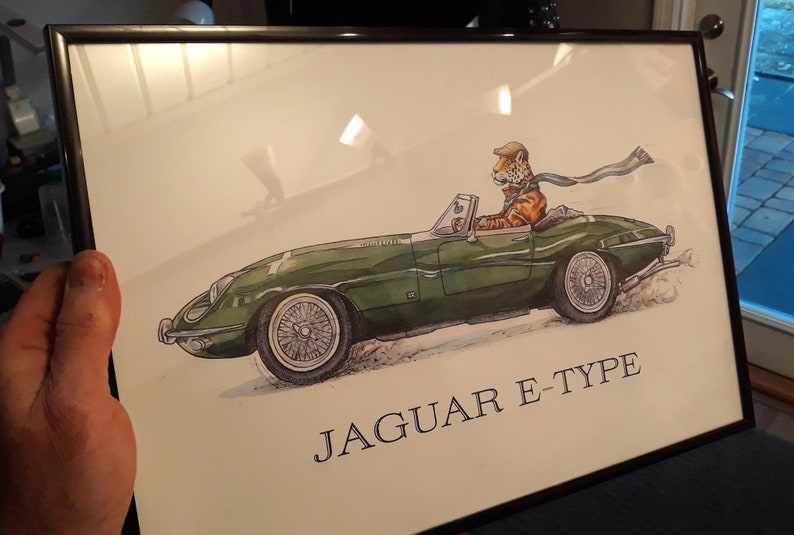 May include: Framed print featuring a green Jaguar E-Type convertible. The illustration shows a tiger wearing a cap and scarf driving the car. The text "JAGUAR E-TYPE" is printed below the car.