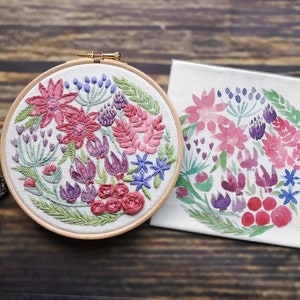 May include: A finished embroidery hoop with a floral design in shades of pink, purple, and green. The design is surrounded by a wooden hoop. A white fabric with a similar floral design is also shown.