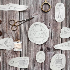 May include: A collection of sewing and embroidery items, including scissors, embroidery hoops, spools of thread, and embroidered designs, are displayed on a wooden surface. A wooden spool and a decorative frame are also present.