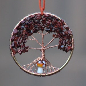 May include: A copper wire tree of life ornament with red gemstone leaves and a glass mushroom at the base.
