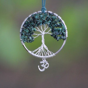 May include: A silver wire wrapped tree of life pendant with green gemstone leaves and an Om symbol charm.