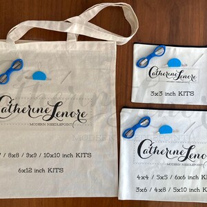 May include: Three white canvas bags with black zipper closures and black text. The largest bag has the text "Catherine Lenore Modern Needlepoint" and lists sizes "7x7 / 8x8 / 9x9 / 10x10 inch KITS" and "6x12 inch KITS". The medium bag has the text "Catherine Lenore Modern Needlepoint" and lists sizes "4x4 / 5x5 / 6x6 inch KITS" and "3x6 / 4x8 / 5x10 inch KITS". The smallest bag has the text "Catherine Lenore Modern Needlepoint" and lists sizes "3x3 inch KITS".