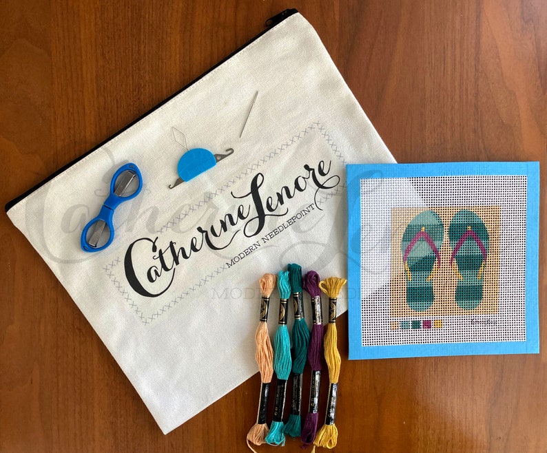 May include: A needlepoint kit with a white canvas bag, blue scissors, a needle threader, embroidery floss in various colors, and a blue canvas with a design of two green and blue flip flops.