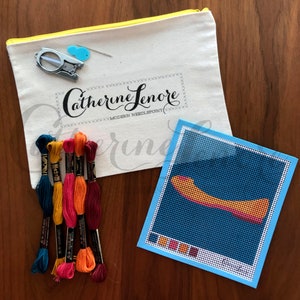 May include: A needlepoint kit with a blue canvas and a colorful design of a shoe. The kit includes floss in various colors and a white canvas bag with the text "Catherine Lenore Modern Needlepoint".