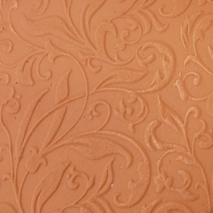May include: A close-up of a terracotta-colored tile with an embossed floral pattern. The pattern is intricate and detailed, with swirling leaves and vines.