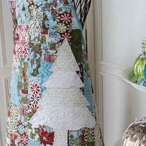 May include: A blue and white patchwork Christmas apron with a white quilted tree design. The apron has a scalloped bottom edge and a white trim.