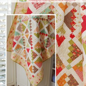May include: A quilt pattern called "Marmalade" by Margot Languedoc Designs. The quilt is made with a variety of fabrics in shades of orange, red, green, brown, and white. The quilt is displayed on a white table with a window in the background.