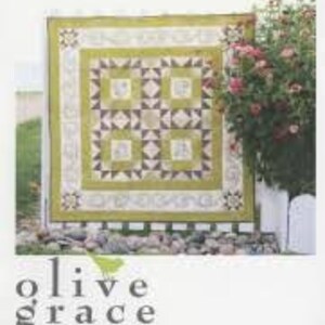 May include: A quilt pattern book titled "Camden Quilt" by Olive Grace Designs. The cover features a green and brown quilt with a floral design. The quilt is displayed against a white picket fence with a green bush in the background.