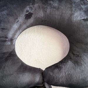 May include: A black, donut-shaped pillow with a central opening. The pillow is made of a soft, plush material and features a ribbon tie closure. The pillow is designed for comfort and support.