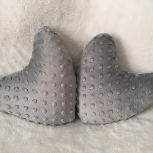 May include: Two gray heart-shaped pillows with a textured surface. The pillows are made of a soft, plush fabric.