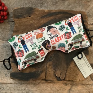 May include: White eye mask with a black elastic strap. The mask is printed with a pattern of characters and phrases from the movie 'Home Alone'. The text includes 'You Serious Clark?' and 'Don't Hog the Nog'.