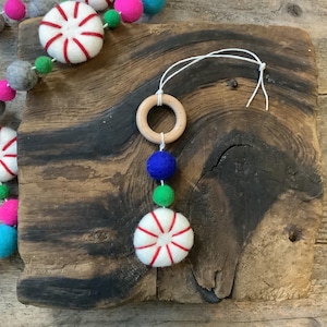 May include: A felt peppermint candy ornament with a wooden ring and blue, green, and white felt balls. The ornament is hanging from a white string.