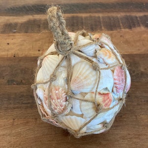May include: A round ball of seashells wrapped in twine. The seashells are a mix of white and pink.